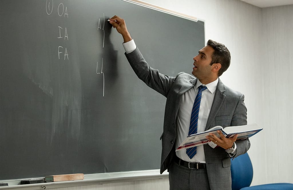 Alex Oliveira holding a textbook and writing on a chalkboard.