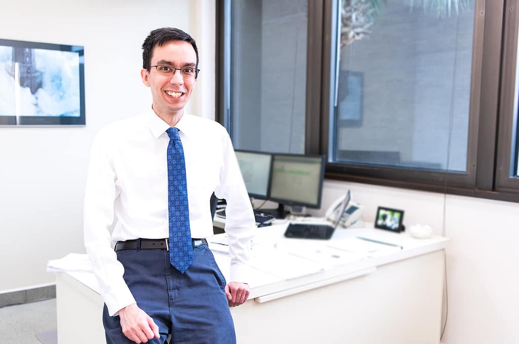 David Valles sitting on the edge of a desk and smiling. 