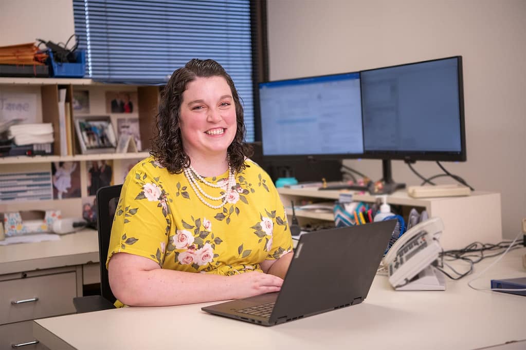 Janae Sparks smiling and sitting at her desk in IT. 