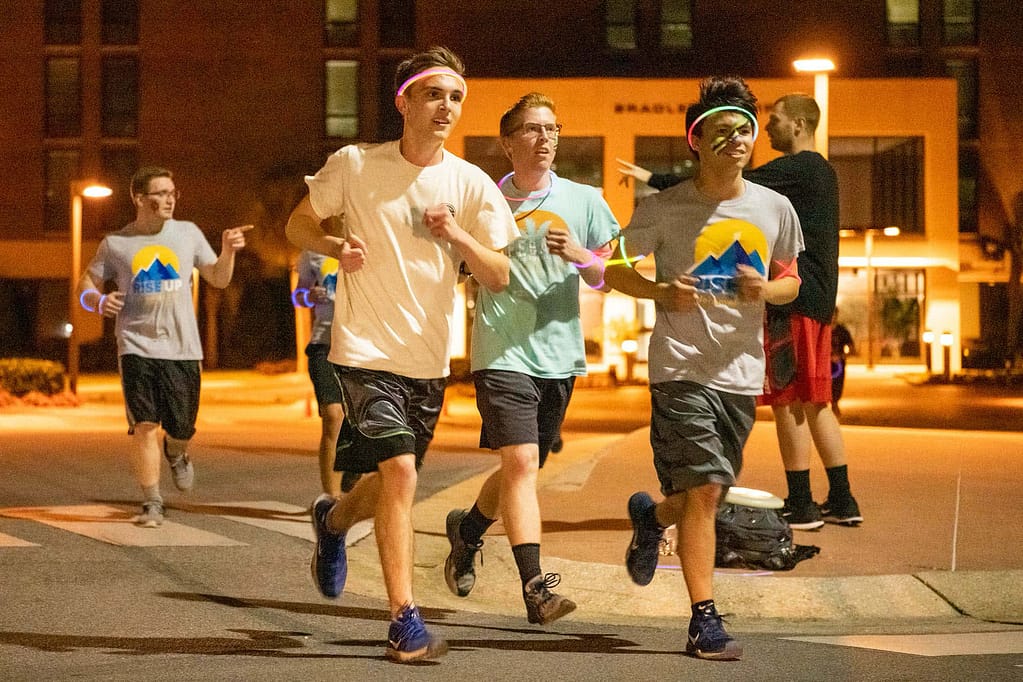 Three guys wearing glow sticks run together.