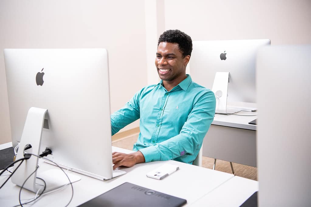 PCC Faculty Tim Golden sitting at a computer and smiling. 