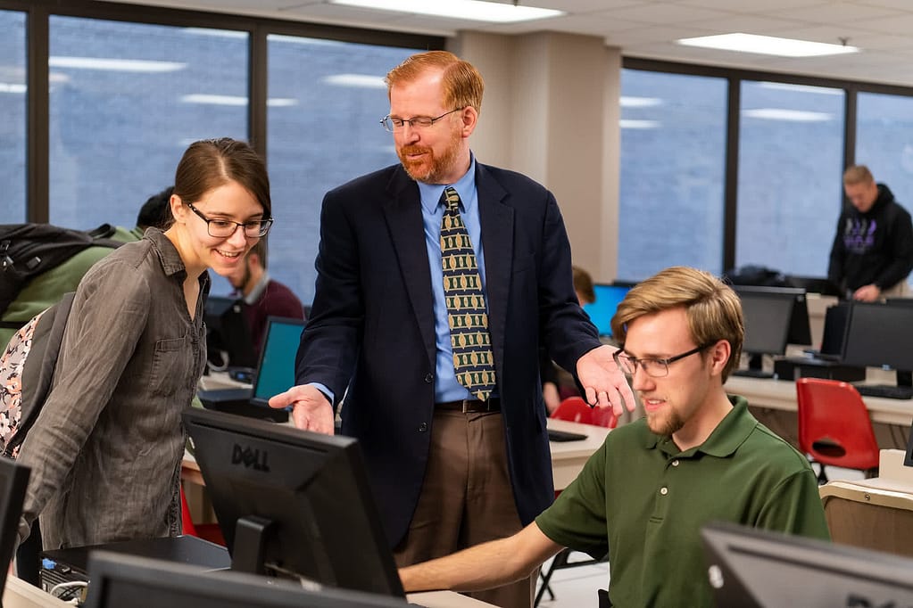 Mike Geary talking to two PCC students at a computer.