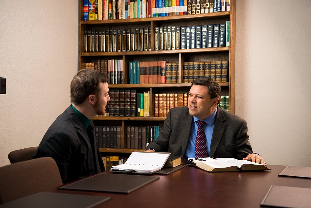 PCC Faculty Dr. Wolf sitting with a Bible and talking to another man wearing a suit. 
