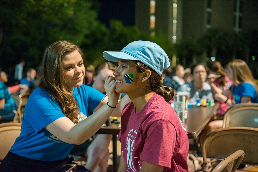One girl paints another girl's face with the flag of Tanzania