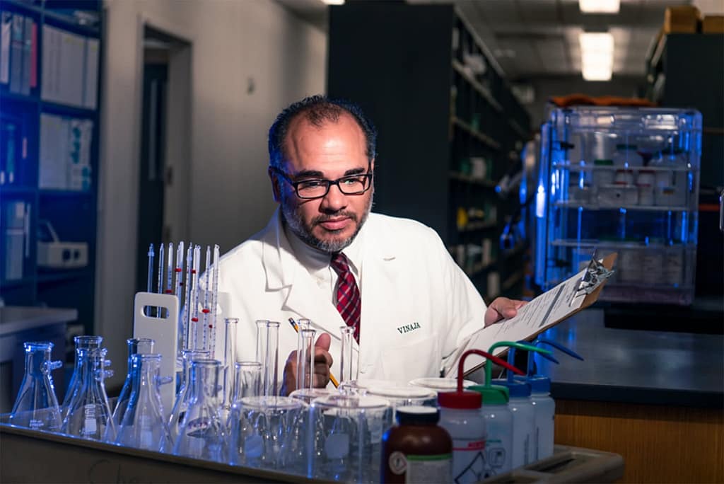PCC Faculty Dr. Sean Vinaja in a lab holding a clipboard. 