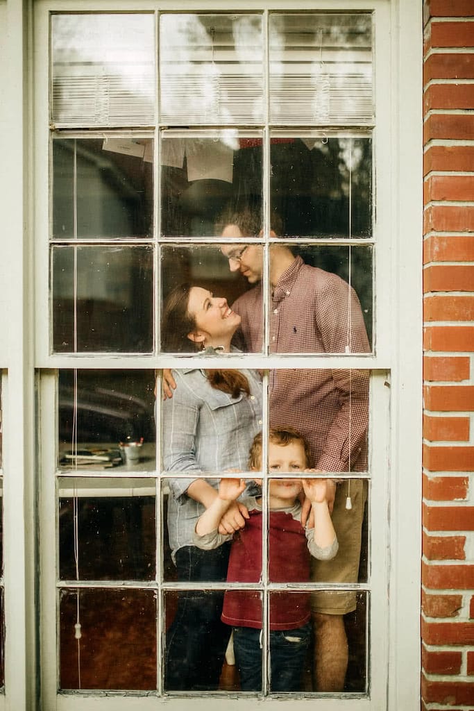 Family smiling at each other and standing in a window.