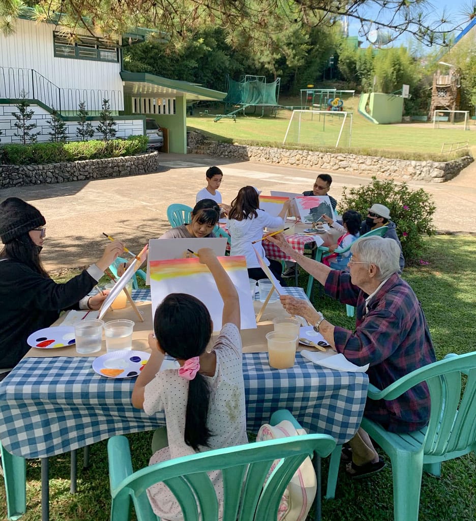 Families in the Philippines sitting at tables and painting. 
