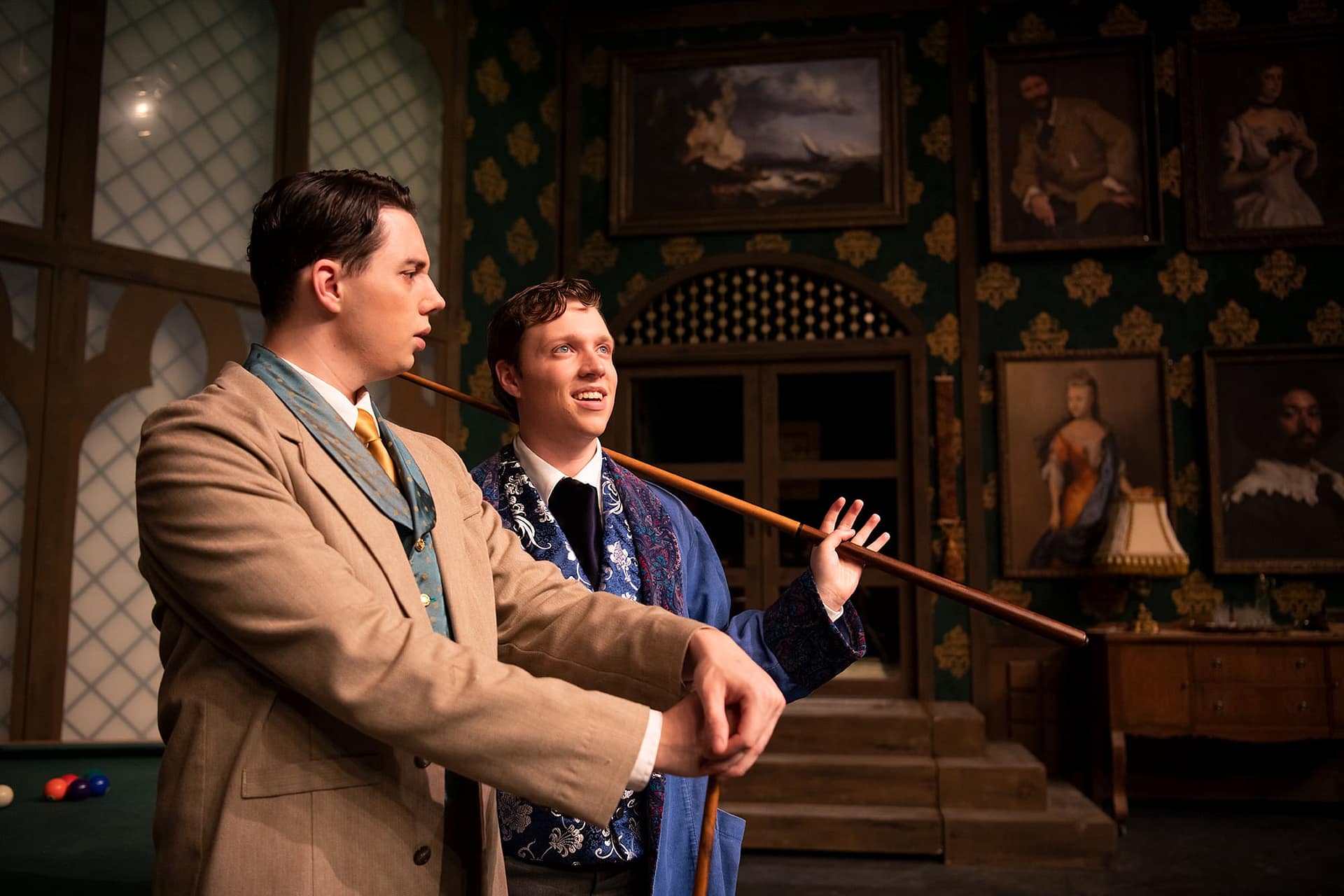 Two men holding pool sticks and looking out. 