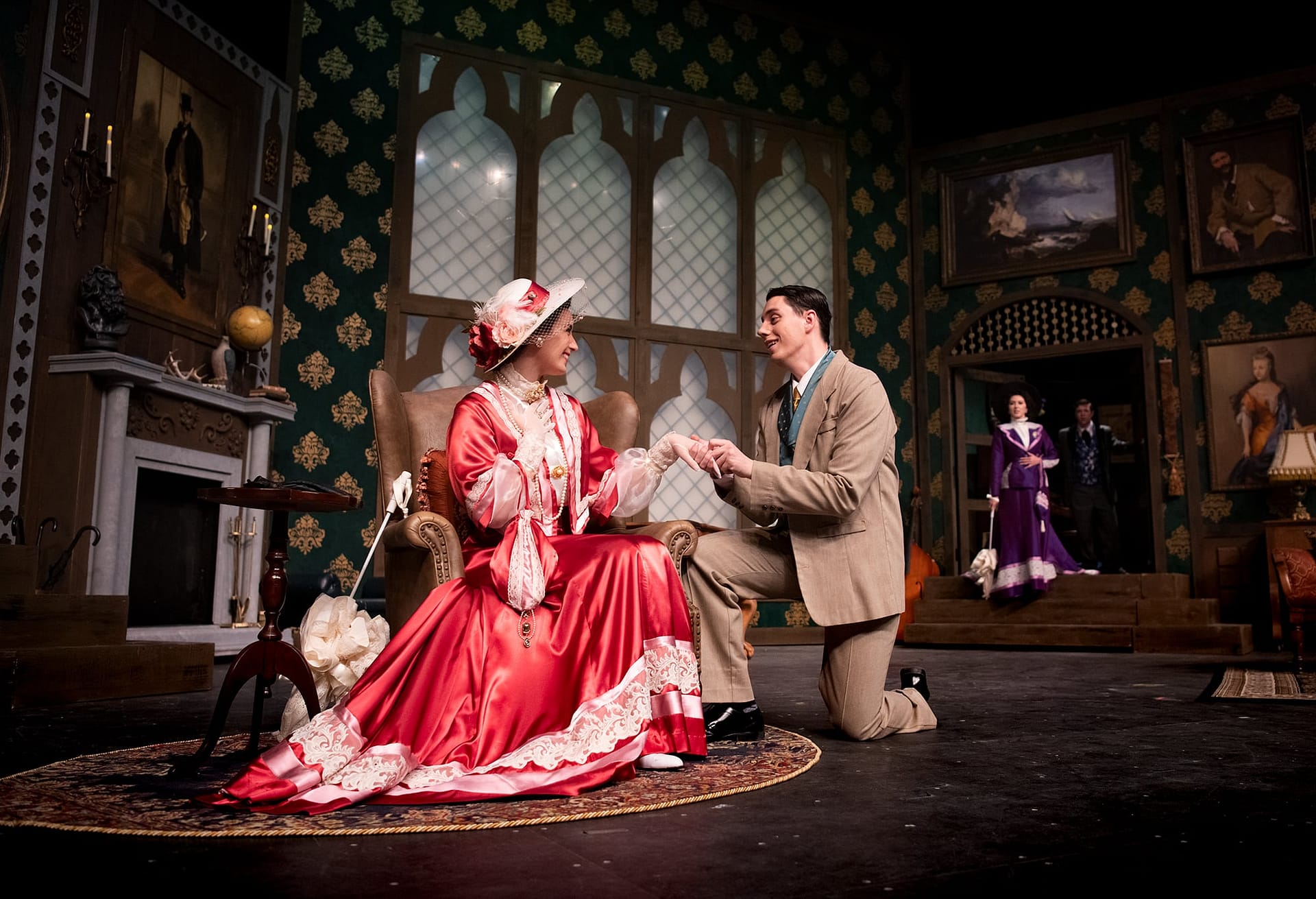 A man kneeling and holding the hand of a woman in a red dress. 
