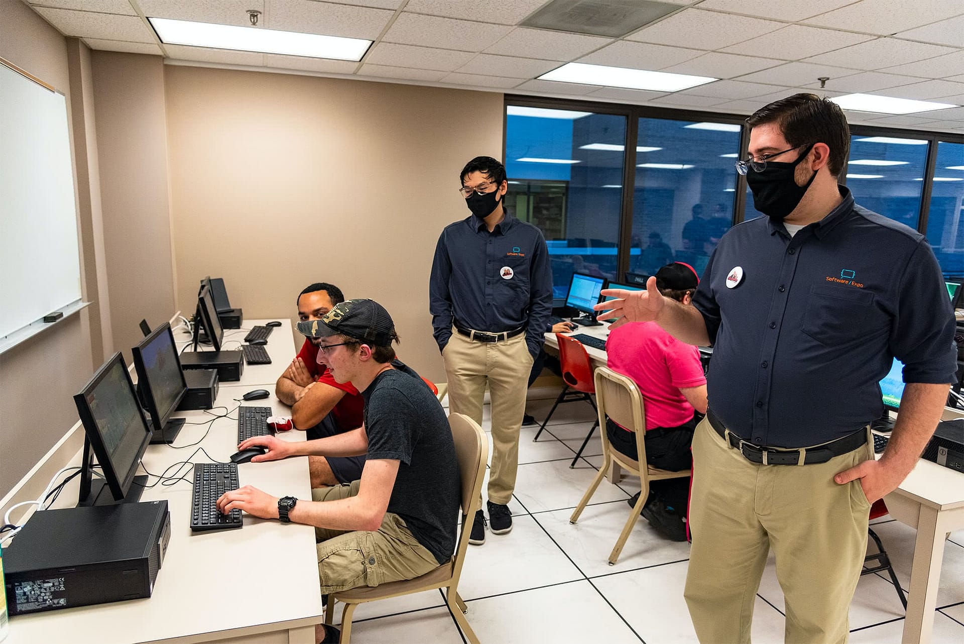 Men standing behind male students that are sitting at computers during the Software Expo.
