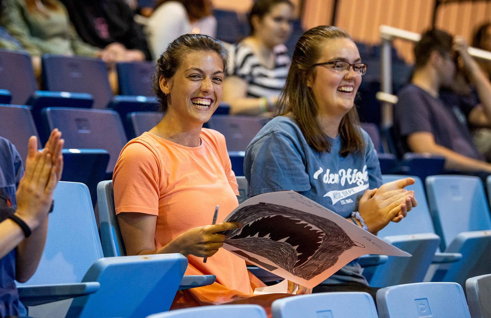 Two female students sitting in bleachers and holding a sign.