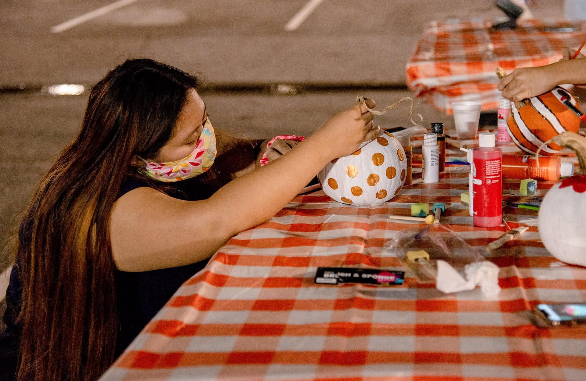 A female student wearing a face covering and decorating a pumpkin.