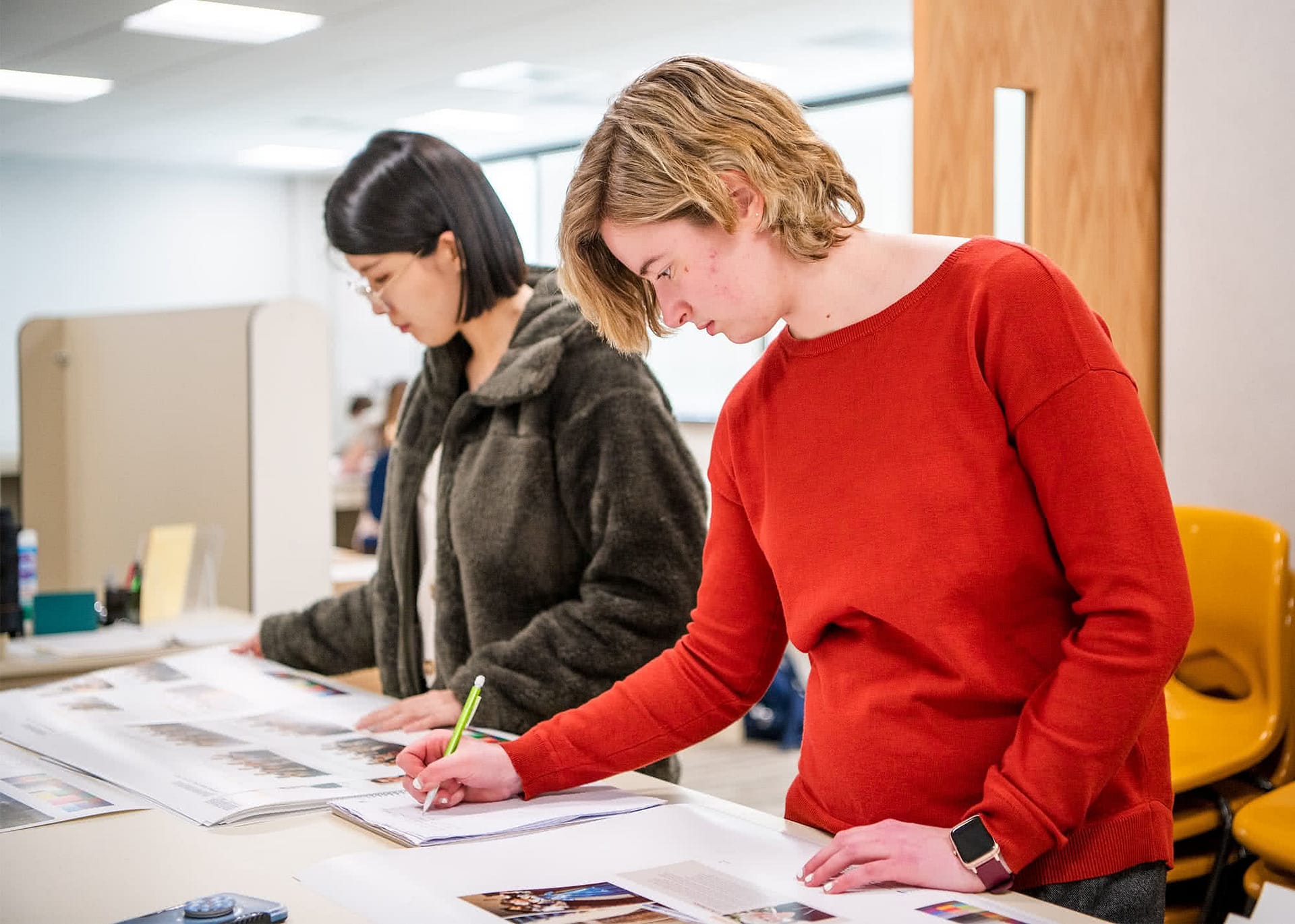 Two female students writing and observing photos for the yearbook. 