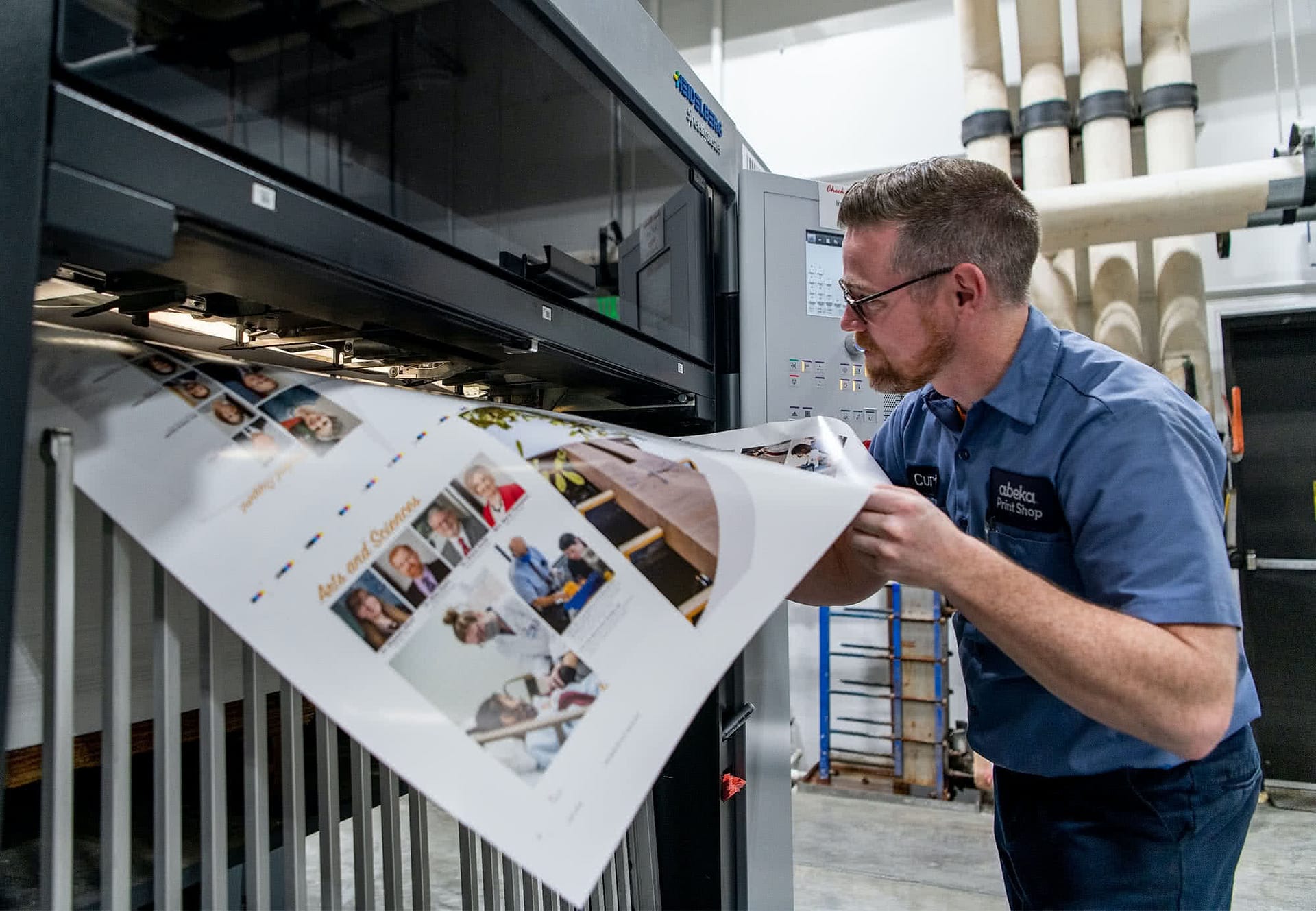 Male Abeka Print Shop staff pulling paper from the printer. 