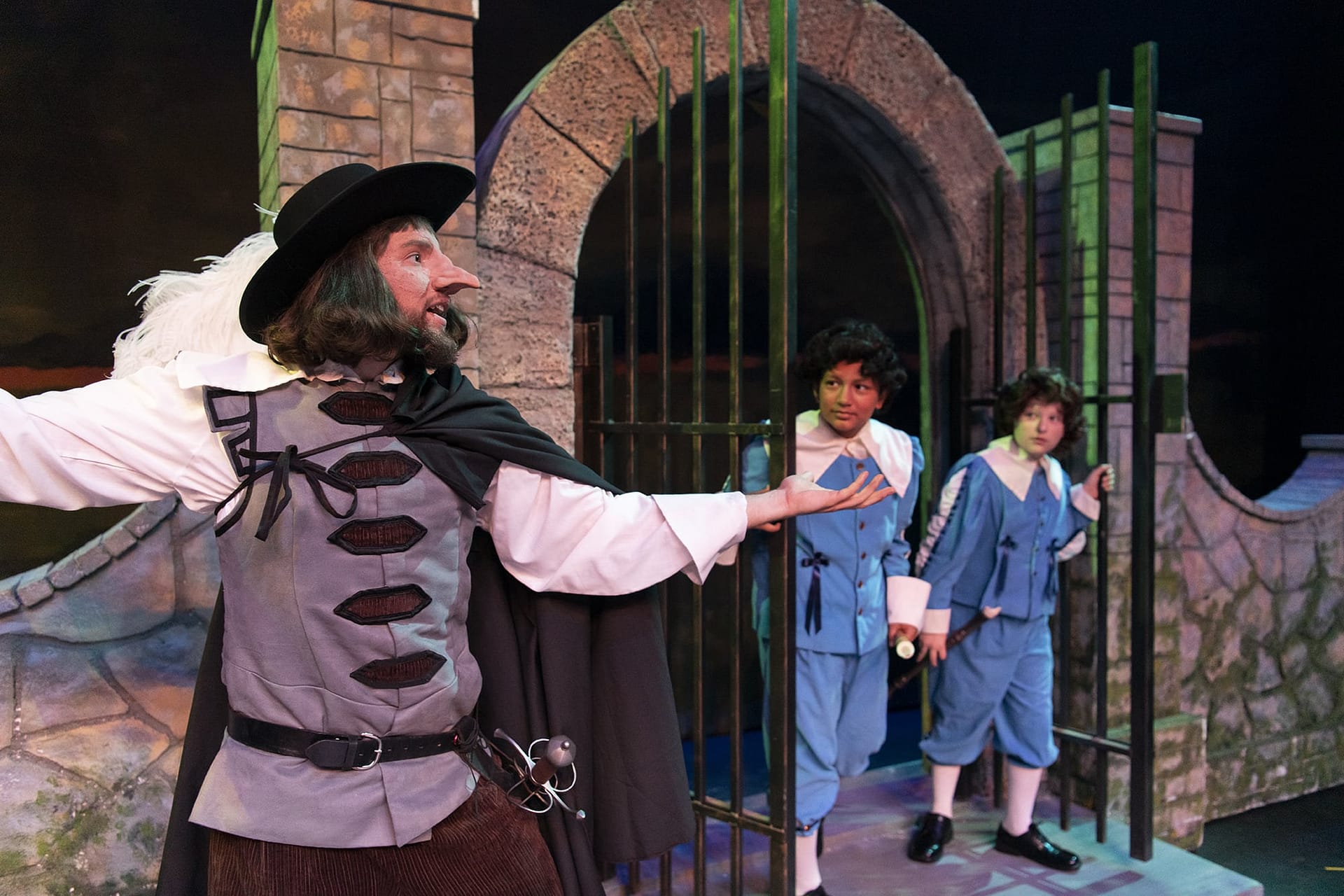 Two boys come through a gate to talk to Cyrano