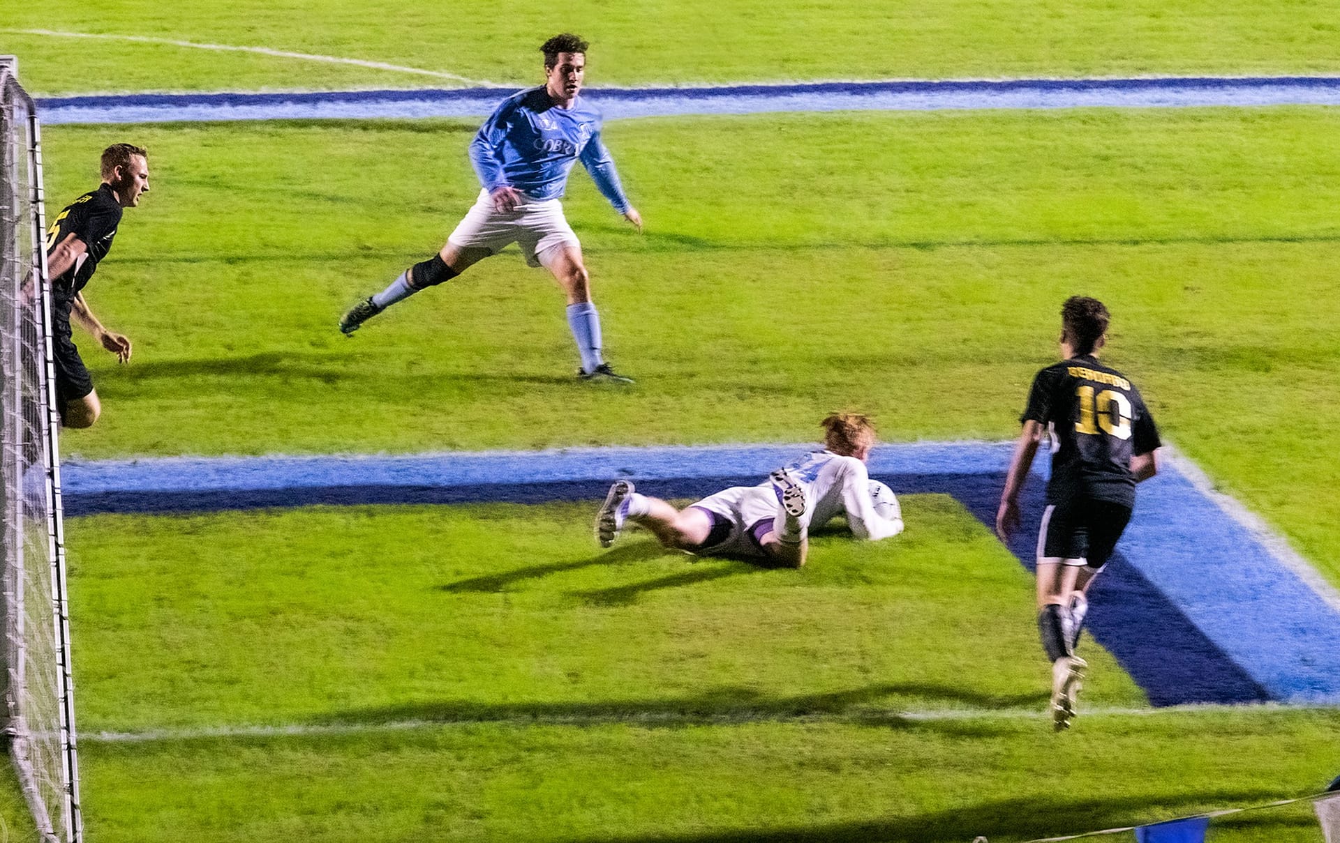 Cobras collegian's goalie holding soccer ball on the ground in front of the goal.