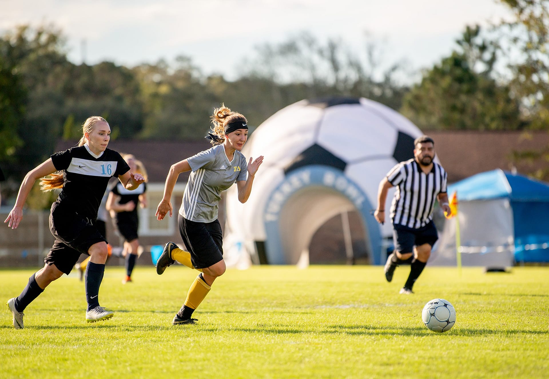 Female student soccer players running after the soccer ball on Eagle's Field.