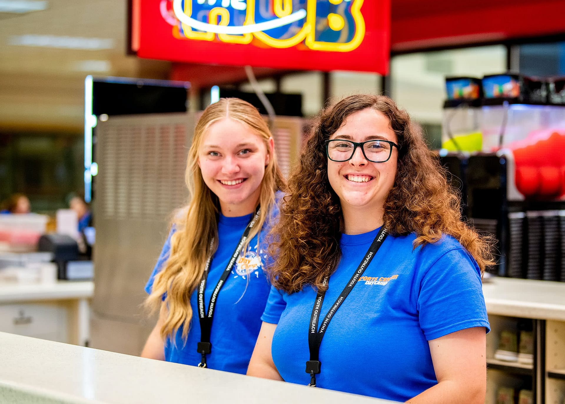 Two female Sports Center Day Camp workers standing at the Hub. 