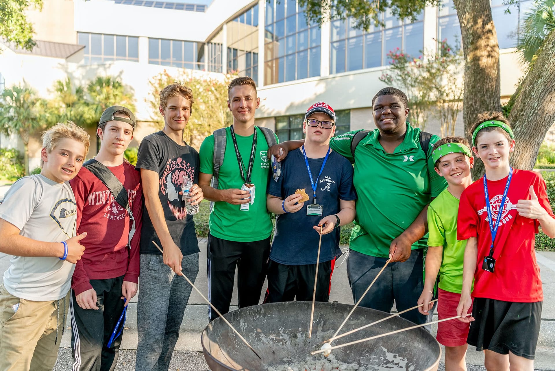 Male Teen Extreme counselors and campers standing around a bonfire and roasting marshmallows. 