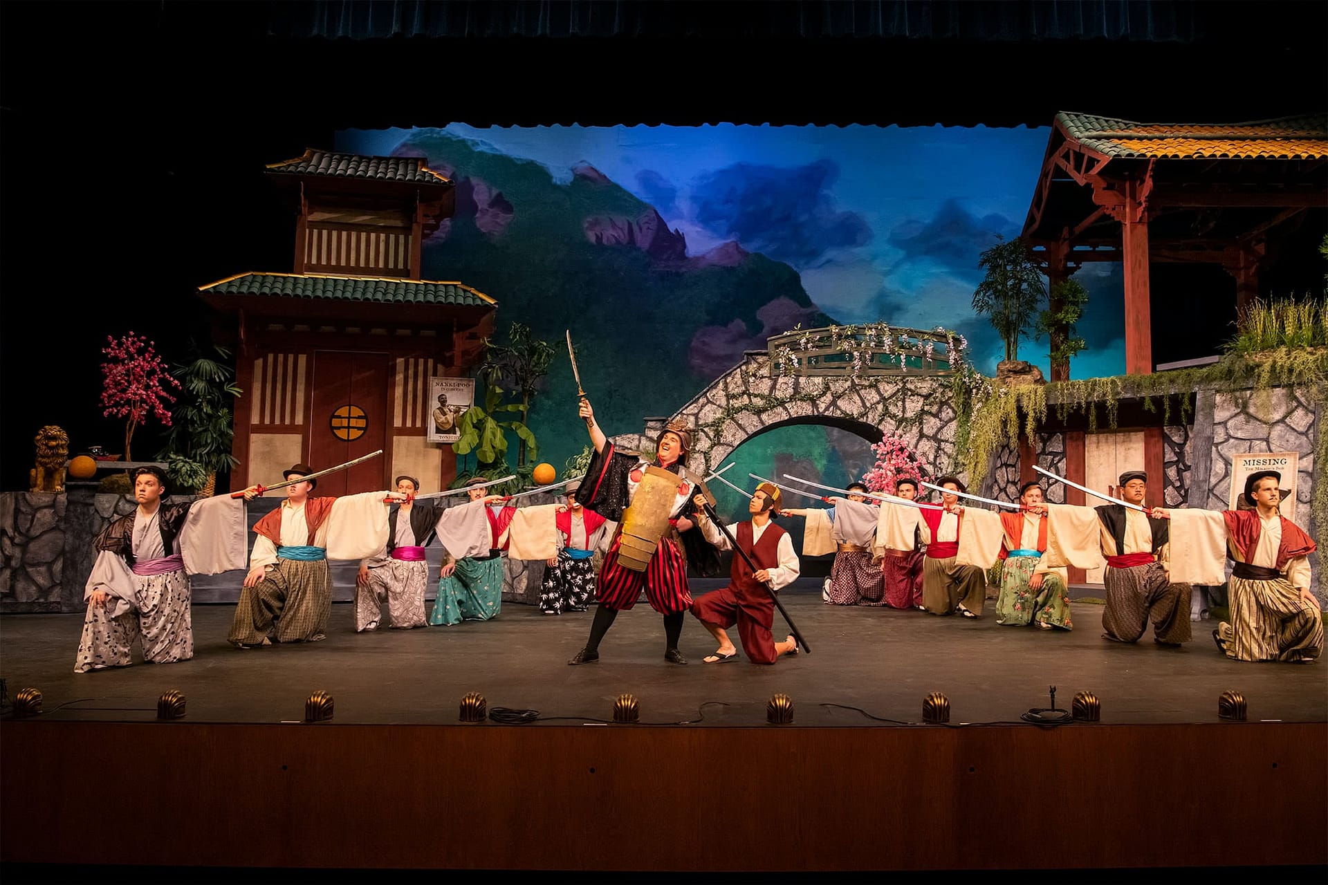 Man holding a sword into the air while other men holding swords kneel down around him.