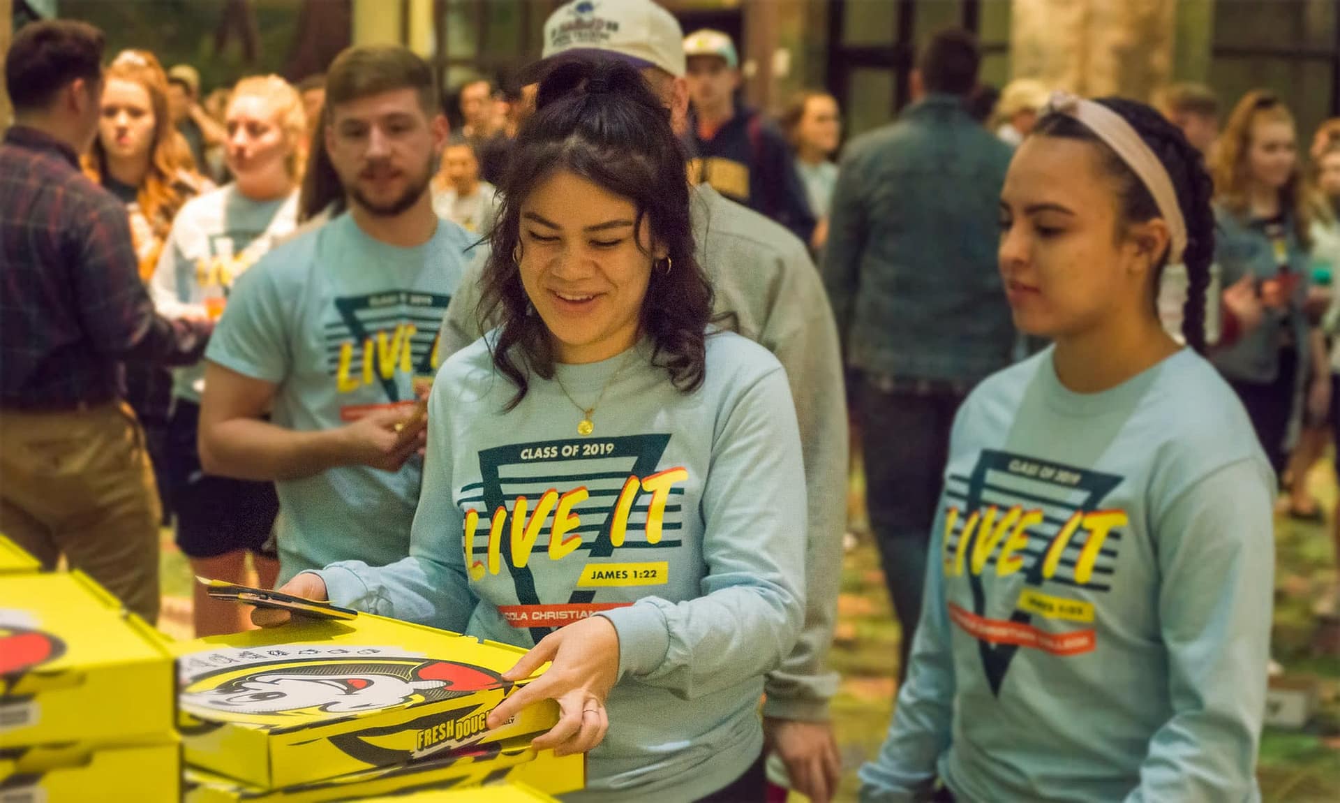 Two female students grabbing a pizza box at their senior class party.