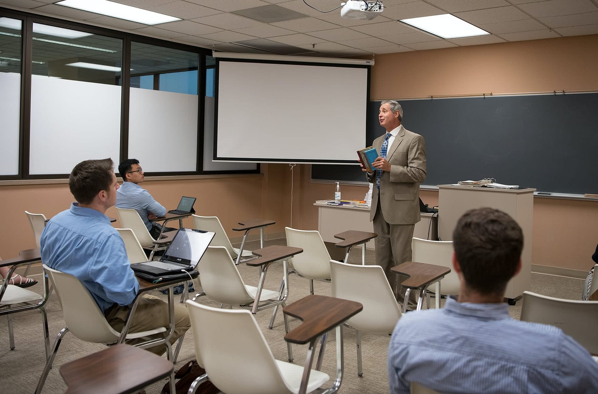 Professor standing at the front of a classroom and lecture a class of graduate students.