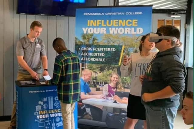 Man helping a boy at a stand while a girl helps a boy with a vr headset. 