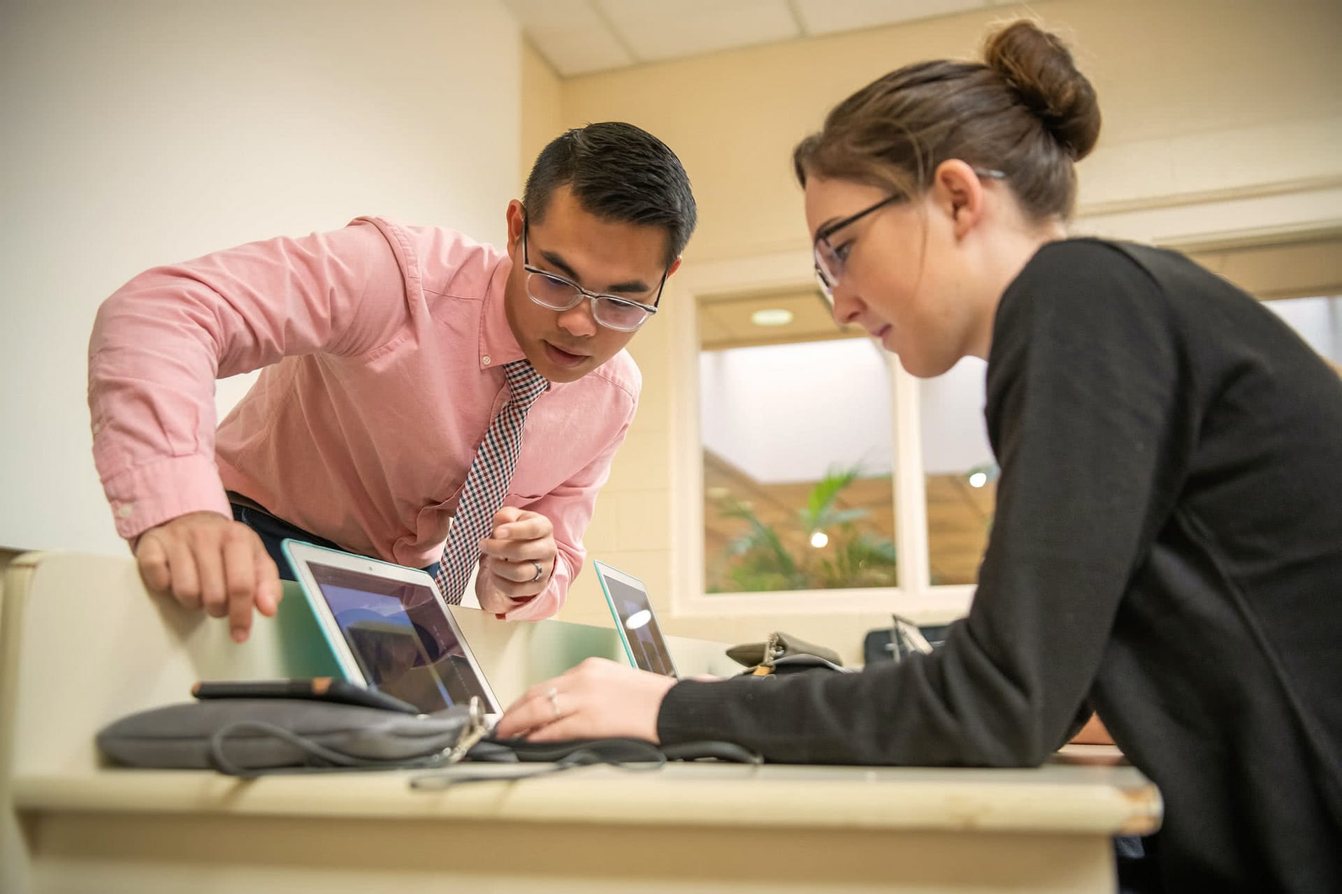 A man helping a female student at her laptop.