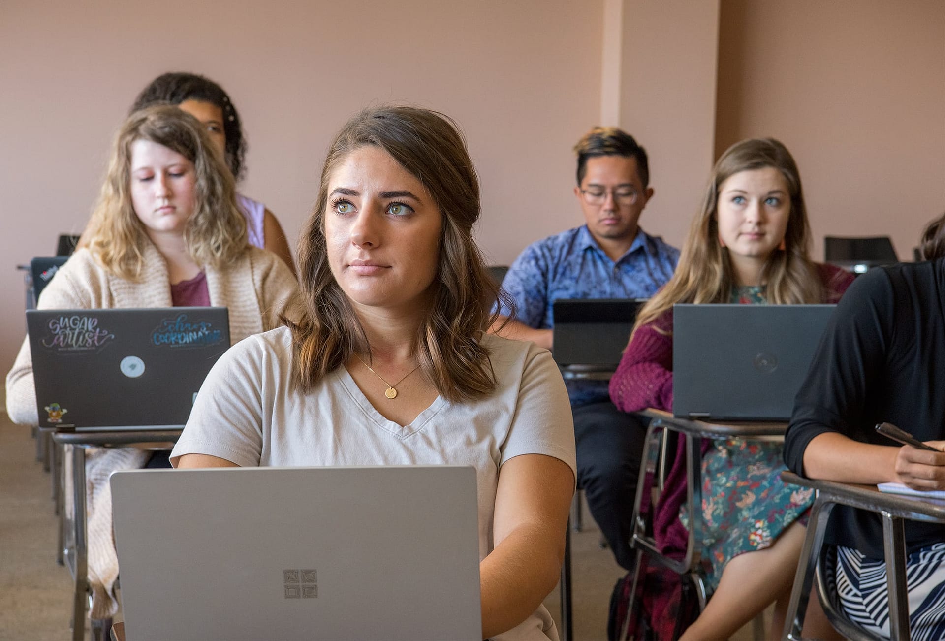 Graduate students sitting with their laptops at desks in a classroom.