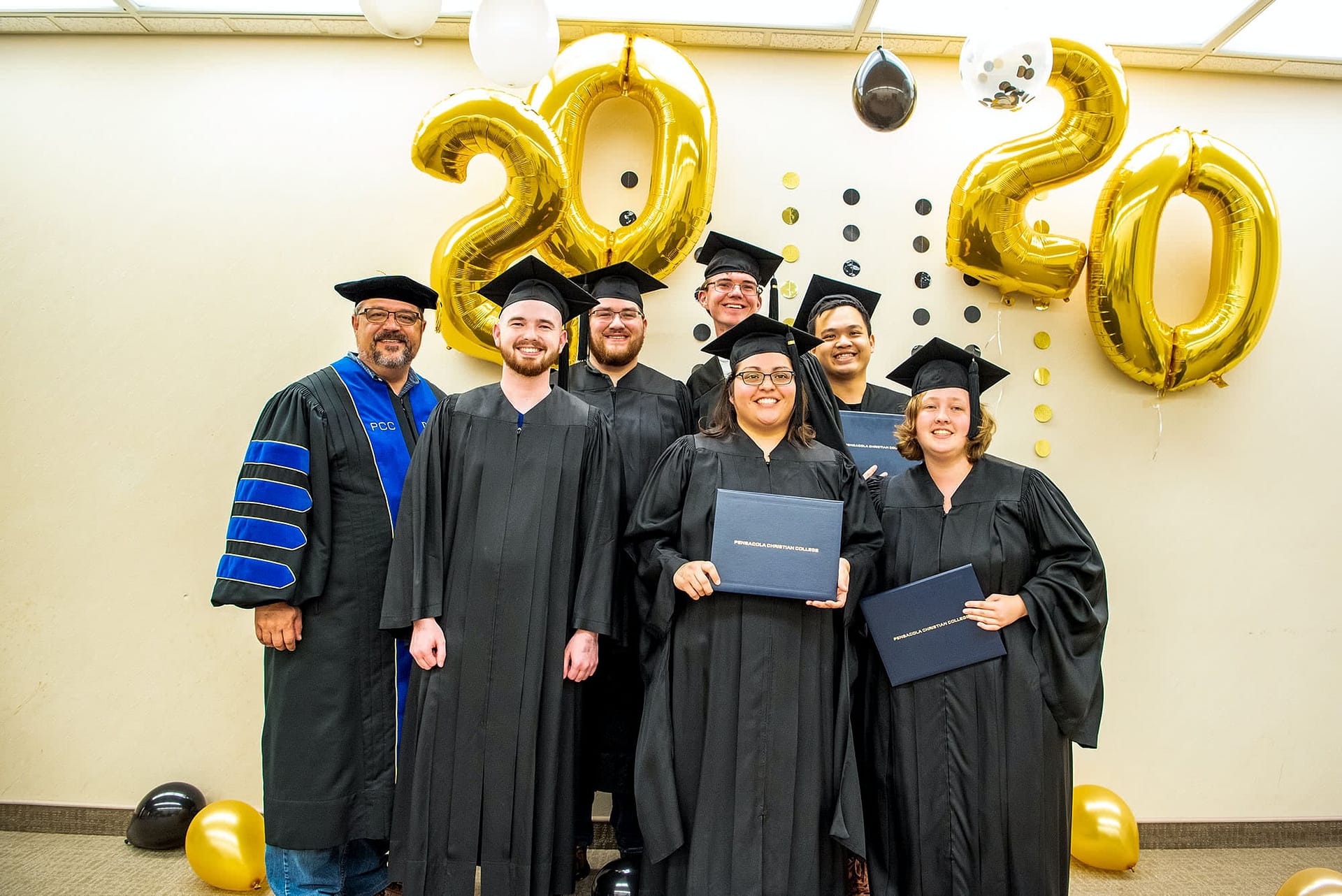 PCC students wearing regalia and posing for a photo with Dr. Shoemaker.