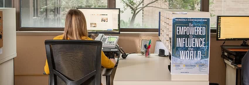 Admissions counselor sitting at a desk and working on a computer. 