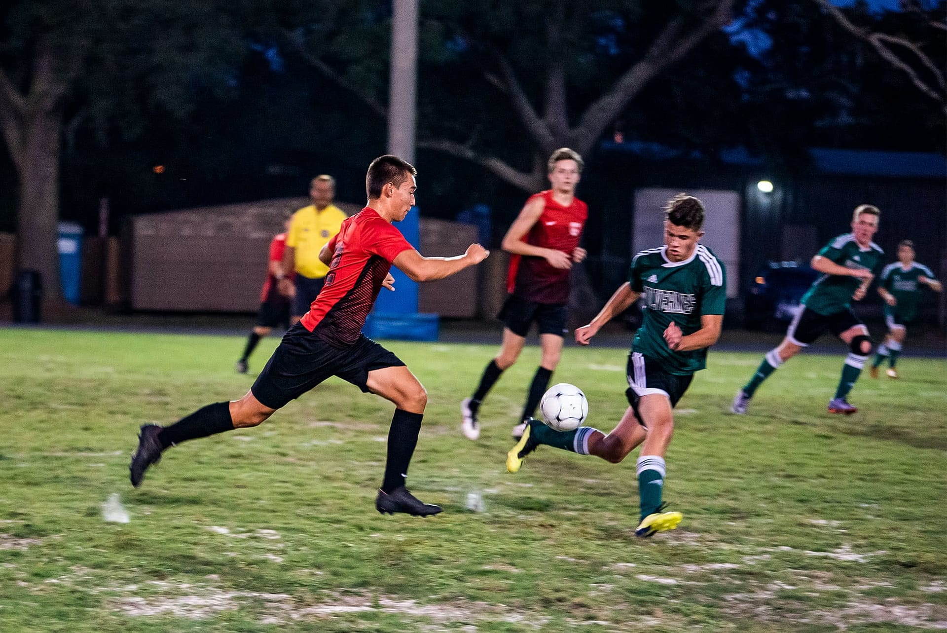Two men's collegian soccer players chasing after a soccer ball. 