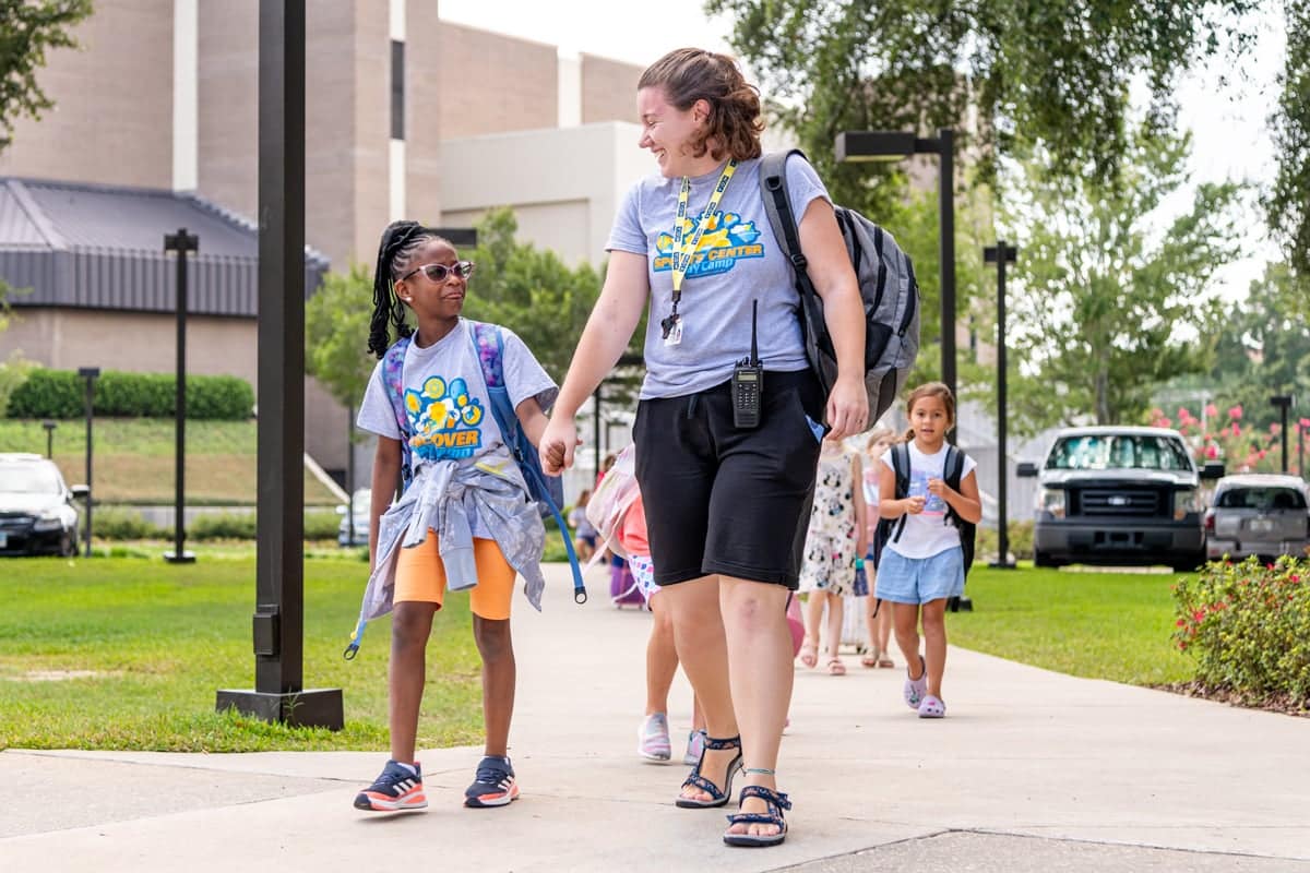 Sports Center Day Camp worker walking with camper
