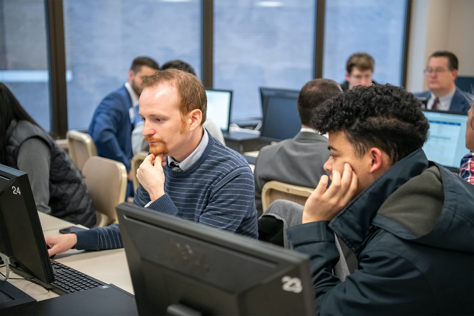 Man sitting at a computer and helping a male student register for classes for new semester.