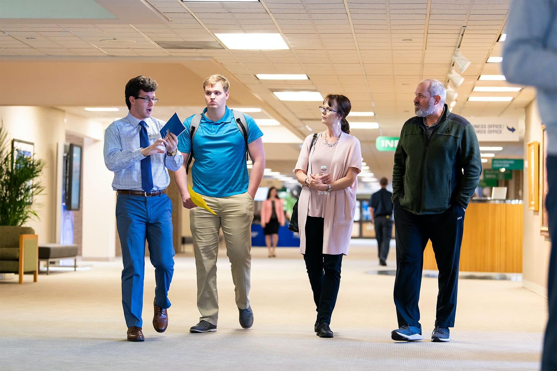 New student walking in academic center with parents and welcome volunteer.