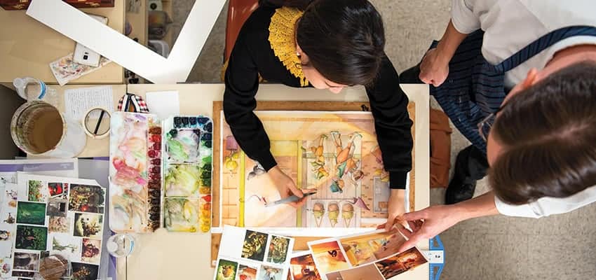 Male professor helping female student as she paints with watercolor.