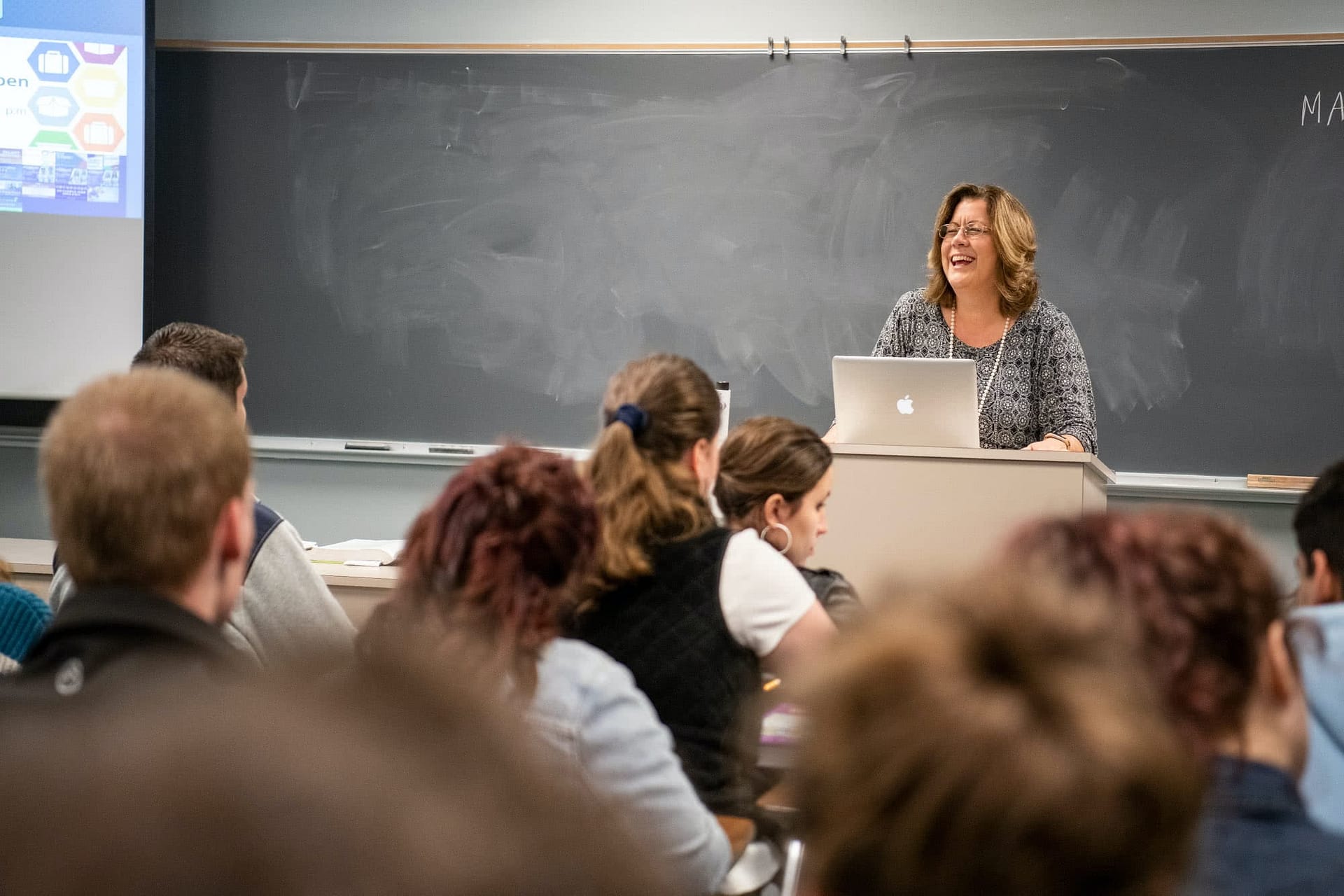 Female teacher standing at the front of the classroom and smiling at her students.