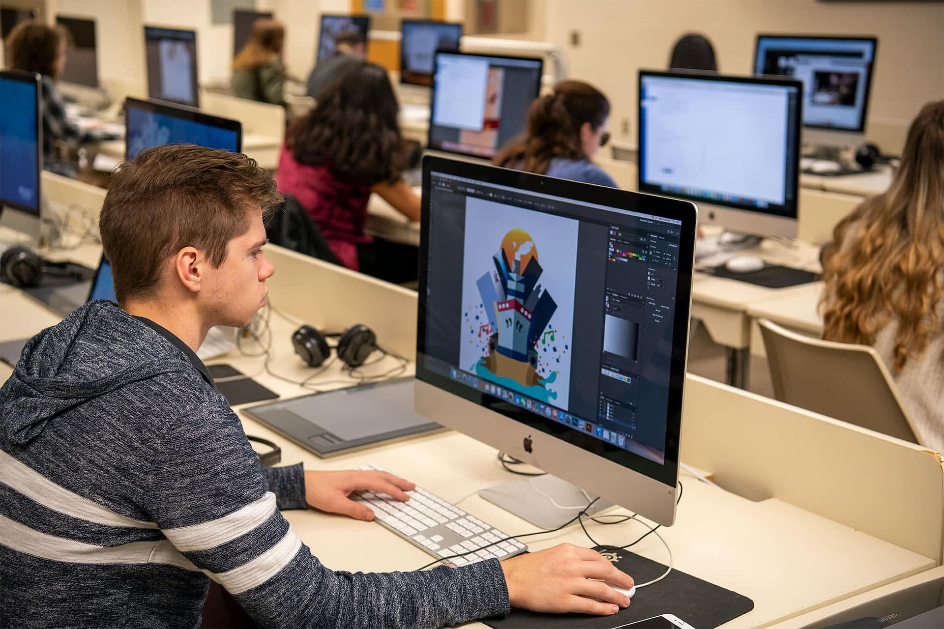 A student works on a illustrated boat and cityscape piece at a computer in the VPA lab