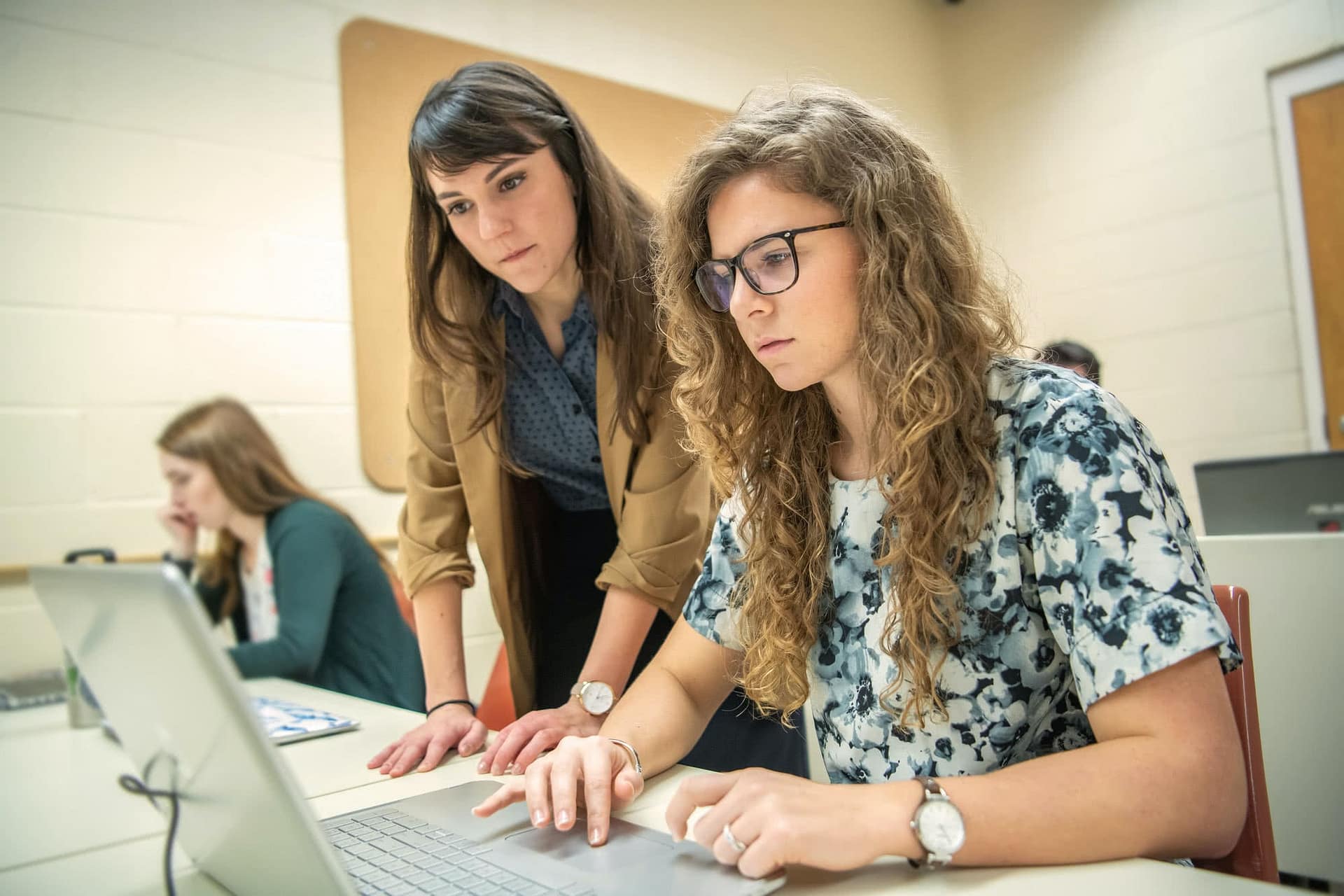 A female teacher helping a student at her laptop.