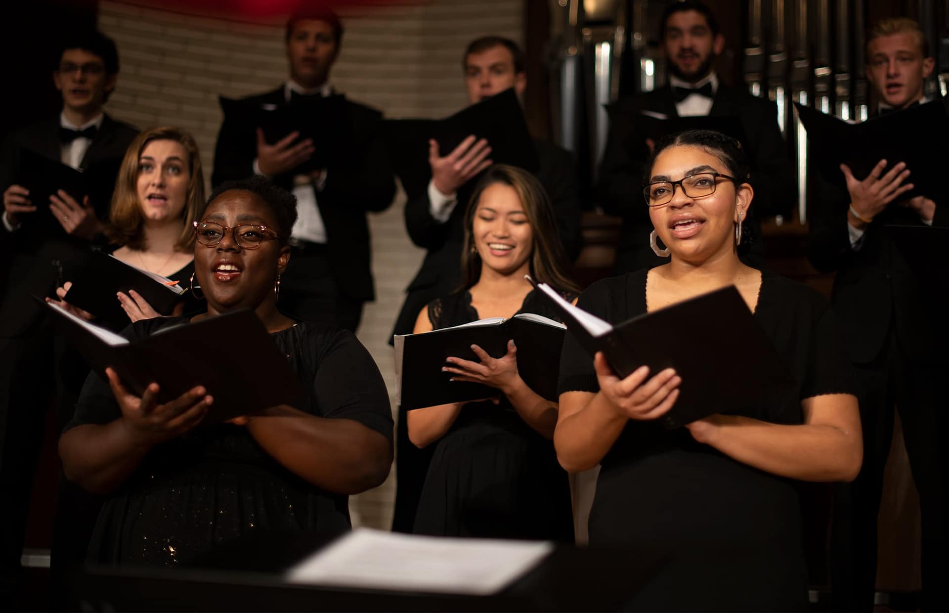 Female students holding song books and singing in the Symphonic Choir.