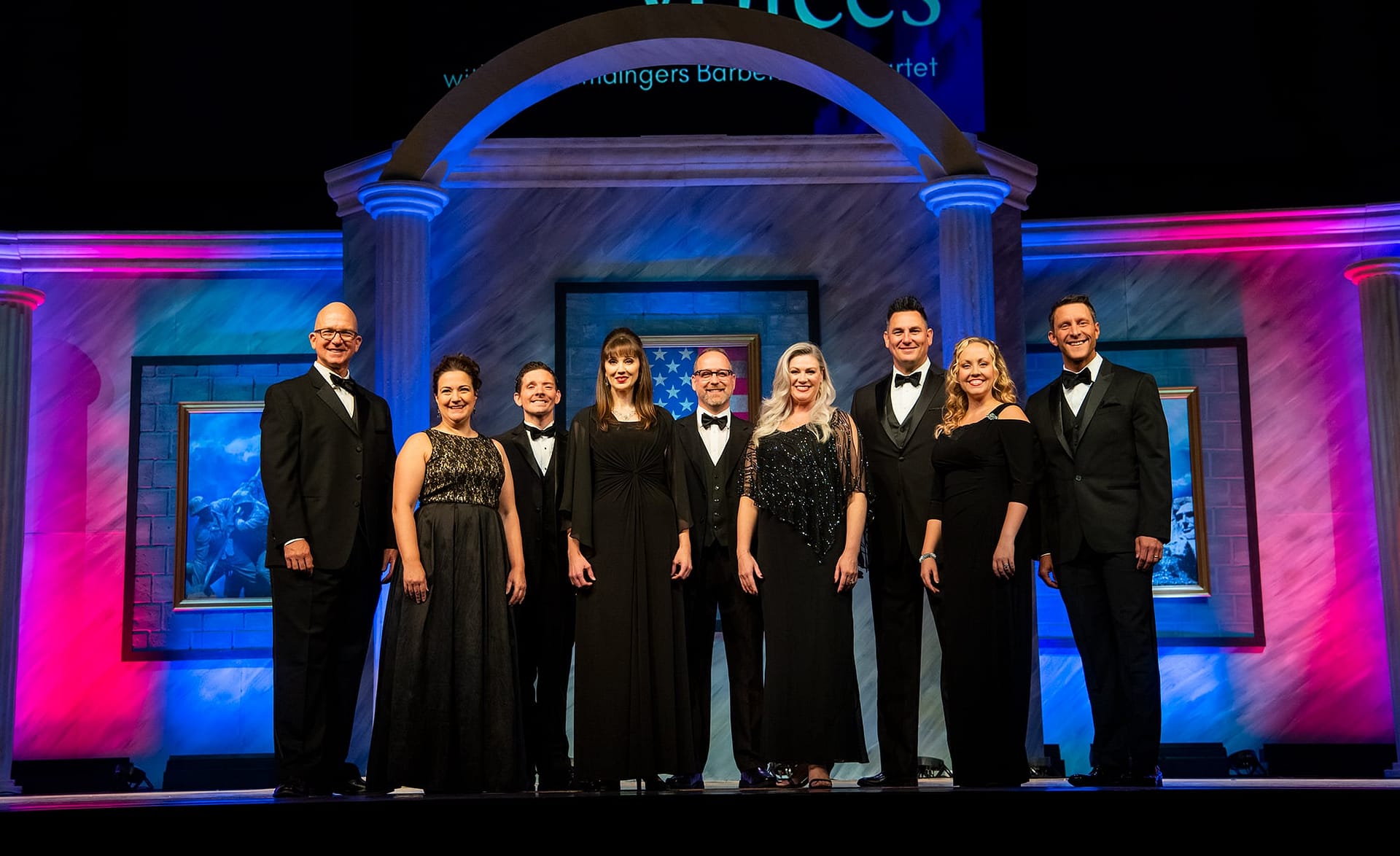 Liberty Voices wearing black suits and dresses standing together as a group and posing for a photo.
