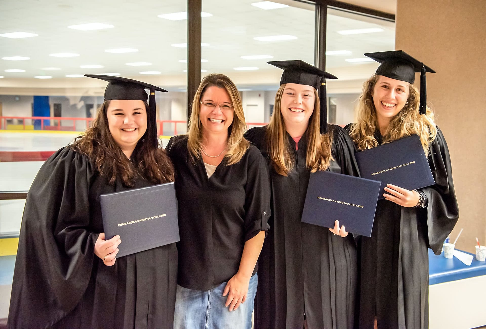 PCC graduates in regalia posing with Mrs. Shoemaker.