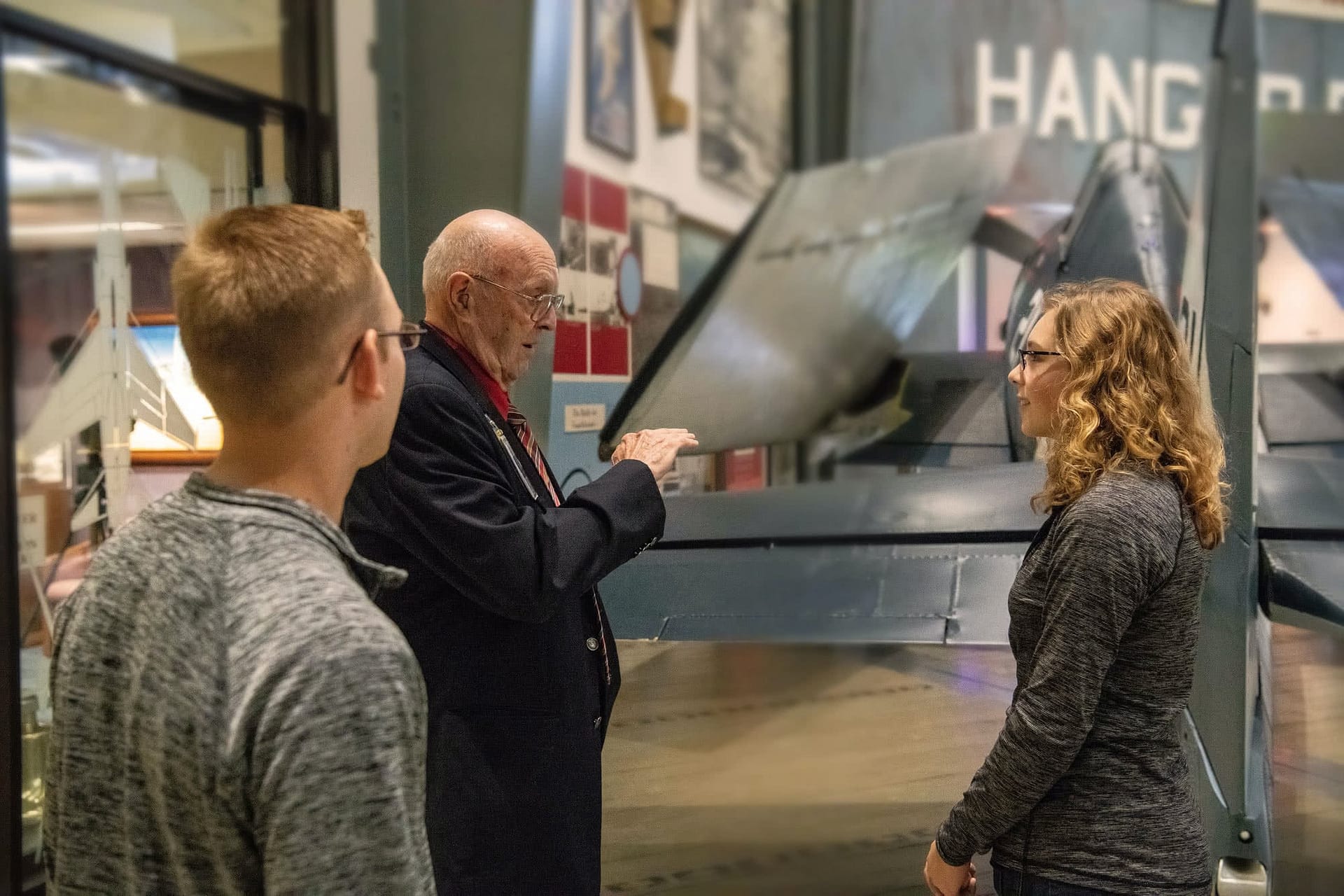 Two students listening to a museum staff at the Naval Aviation Museum.