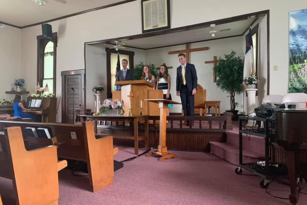Four proclaim singers standing on a church's stage and singing together. 