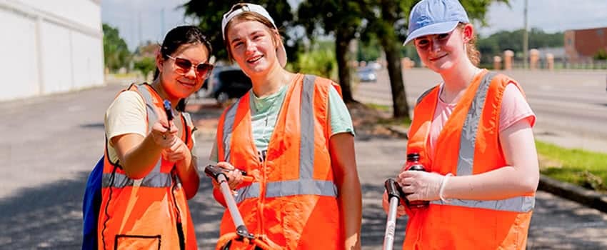 Three girls wearing neon orange vests pose for a picture