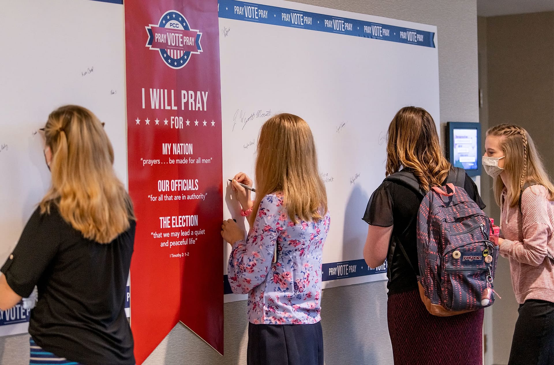 Three female PCC students writing on the Student Body "Pray, Vote, Pray" board.