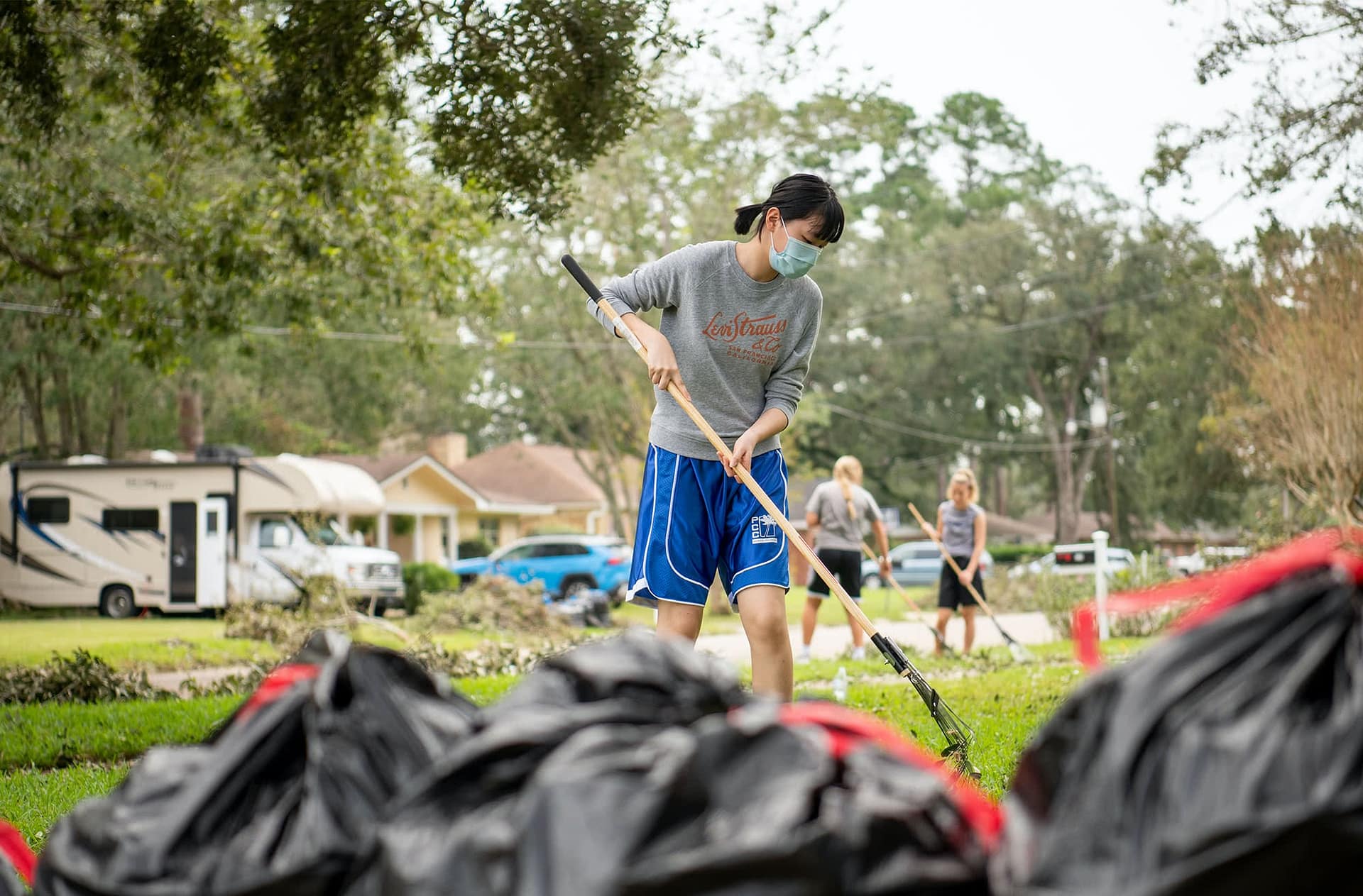 A female student rakes debris in a nearby neighborhood