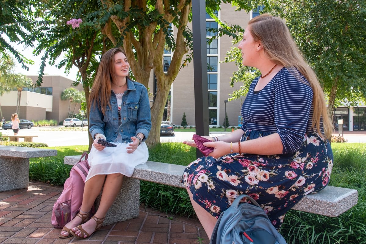 Two PCC girls sitting on a bench outside by Campanile