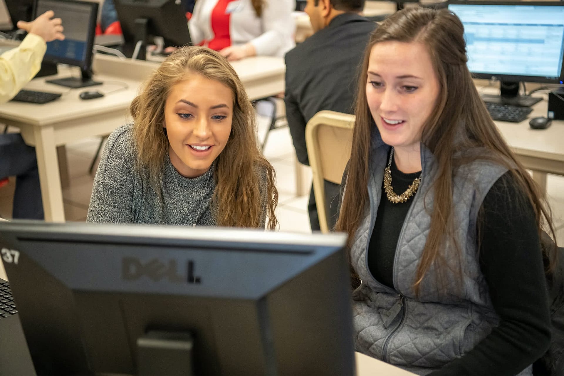 A woman sitting at a computer and helping a female student register for new semester classes.