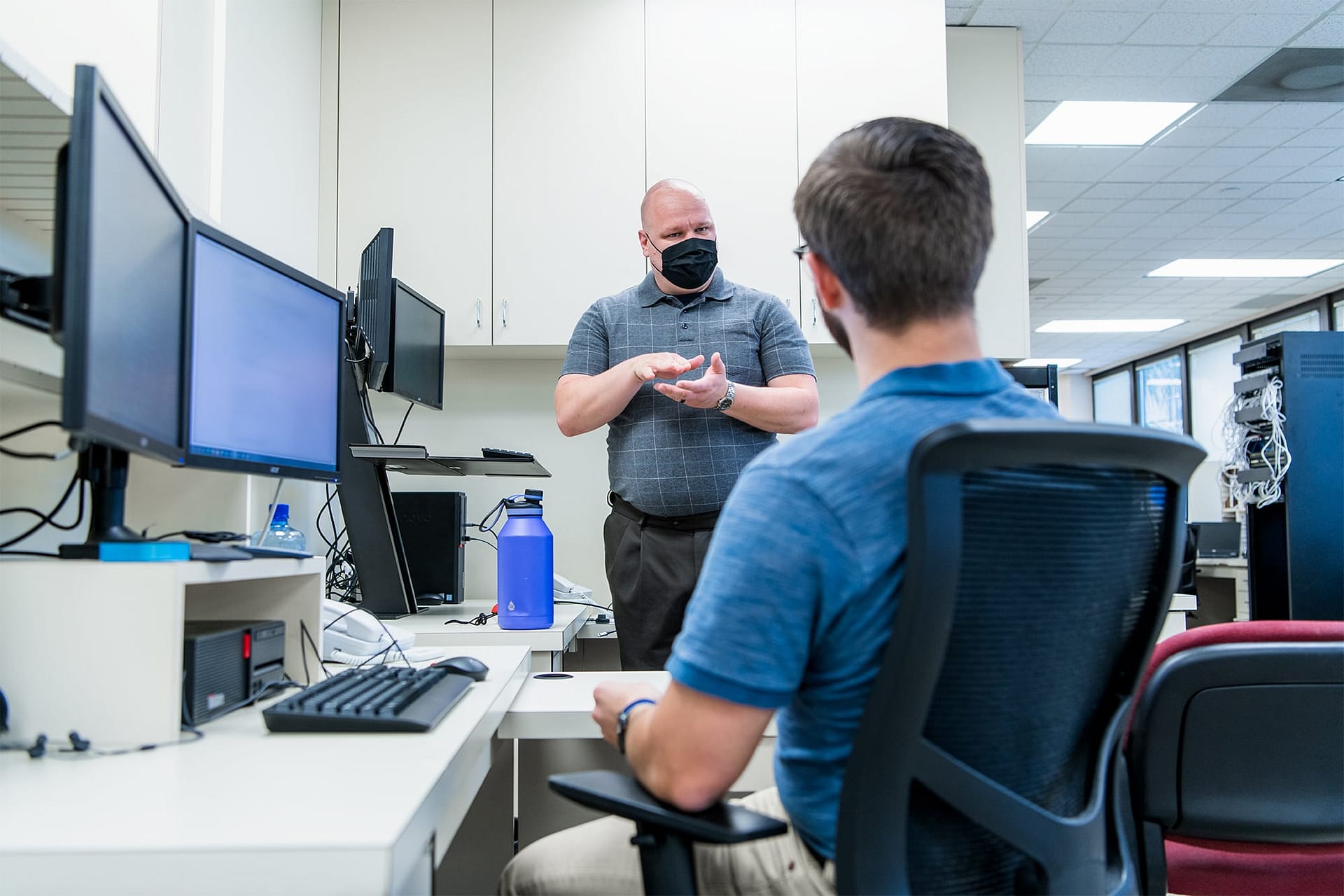 Two IT staff members speak at their desks.